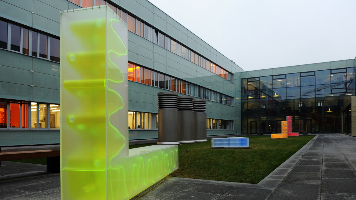 Gebäude der Mathematisch-Naturwissenschaftlichen Fakultät der Universität Potsdam. (Credit: UP) Blick in den Innenhof der Mathematisch-Naturwissenschaftlichen Fakultät der Universität Potsdam. Im Vordergrund ein L-Förmiges neongelbes Kunstobjekt mit wellenförmiger Innenstruktur.