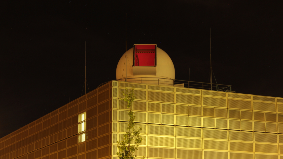 Teleskopkuppel der Universität Potsdam (Credit: R.Hainich/UP) Das golden leuchtende Gebäude der Matematisch-Naturwissenschaftlichen Fakultät der Universität Potsdam bei Nacht, oben auf dem Dach ist die Teleskopkuppel mit geöffnetem Kuppelspalt zu sehen.