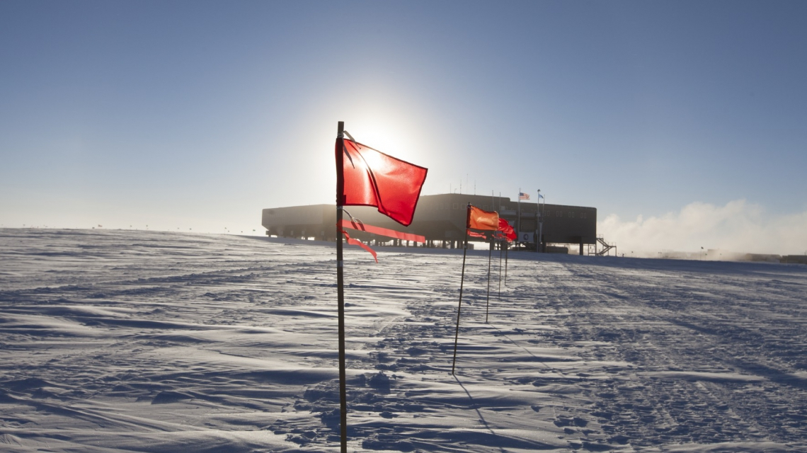 Markierte Straße vom IceCube Labor zur Südpolstation im Sommer. (Credit: Freija Descamps/NSF, 2011) Mit Flaggen markierte Straße vom IceCube Labor zur Südpolstation im Sommer. (Credit: Freija Descamps/NSF, 2011)